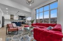 Expansive great room featuring soaring ceilings, a full wall of windows, recessed lighting, wood-finish flooring, and a kitchen with an island, pendant lighting, and built-in cabinetry - 1409 Graydon Hill Way Sw, Edmonton, AB 