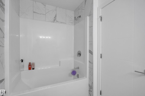 White bathtub and shower combination with white and gray veined tile surround - 1409 Graydon Hill Way Sw, Edmonton, AB 