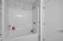 White bathtub and shower combination with white and gray veined tile surround - 