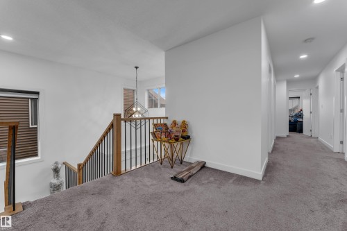 Upper-level landing featuring plush carpeting, recessed lighting, wood-finish stair railings with black balusters, a geometric pendant light fixture, and multiple windows with horizontal blinds - 1409 Graydon Hill Way Sw, Edmonton, AB 