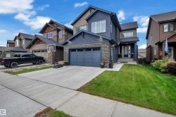 Multi-level residence featuring a stone and siding exterior, an attached garage, a paved driveway, and a front lawn - 