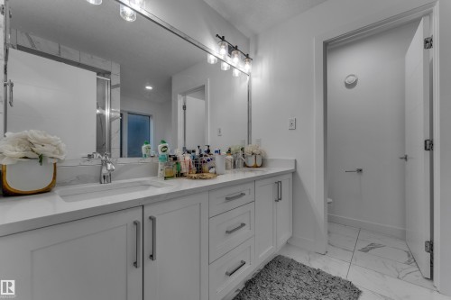 Dual undermount sinks, expansive vanity with white shaker-style cabinetry, chrome hardware, and large wall-mounted mirror - 1409 Graydon Hill Way Sw, Edmonton, AB 
