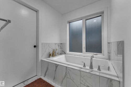 Built-in soaking tub with polished chrome fixtures, surrounded by white-veined tile and a privacy window - 1409 Graydon Hill Way Sw, Edmonton, AB 
