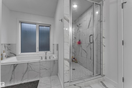 Bathroom featuring a built-in tub with deck-mounted fixtures, a glass-enclosed shower with tile surround, and tile flooring - 1409 Graydon Hill Way Sw, Edmonton, AB 