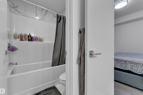 Tub and shower combination with white surround, integrated shelving, and a decorative tile accent wall - 1409 Graydon Hill Way Sw, Edmonton, AB 
