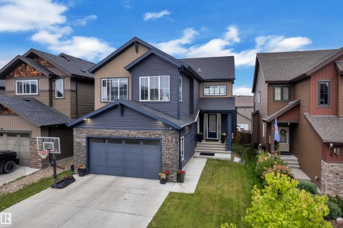 Two-story residence featuring a stone-clad garage, siding exterior, attached garage, concrete driveway, and a covered front entry - 1409 Graydon Hill Way Sw, Edmonton, AB 