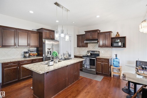 Kitchen featuring wood-finish flooring, dark wood cabinetry, light-toned countertops, a central island with a sink, and stainless steel appliances - 1523 36 Avenue Nw, Edmonton, AB 
