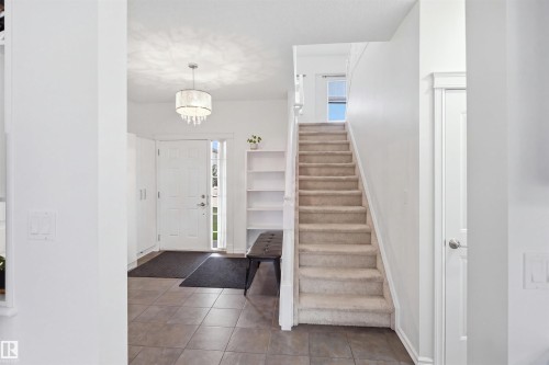 Tiled entry flooring, carpeted staircase, built-in shelving, white paneled door, and a decorative pendant light fixture - 1523 36 Avenue Nw, Edmonton, AB 