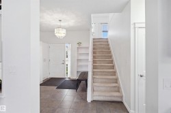 Tiled entry flooring, carpeted staircase, built-in shelving, white paneled door, and a decorative pendant light fixture - 