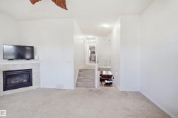 Carpeted flooring throughout, with a tiled fireplace featuring a mantel, and a multi-level layout with a carpeted staircase and white railing - 
