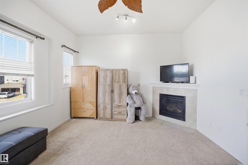 Carpeted room featuring a corner fireplace with a tiled surround and mantel, multiple windows with blinds, and a ceiling fan with integrated lighting - 1523 36 Avenue Nw, Edmonton, AB 