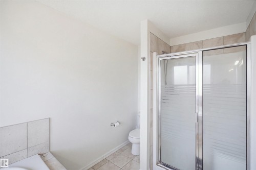 Tiled shower enclosure with sliding frosted glass door, white toilet, and light-toned floor tile - 1523 36 Avenue Nw, Edmonton, AB 