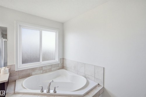 Corner soaking tub with deck-mounted chrome fixtures, frosted glass window, and tiled surround - 1523 36 Avenue Nw, Edmonton, AB 