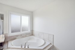 Corner soaking tub with deck-mounted chrome fixtures, frosted glass window, and tiled surround - 