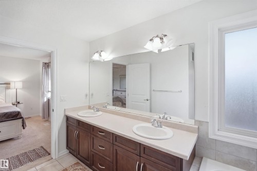 Double vanity with integrated sinks, expansive wall mirror, dark wood-finish cabinetry, and overhead sconce lighting - 1523 36 Avenue Nw, Edmonton, AB 
