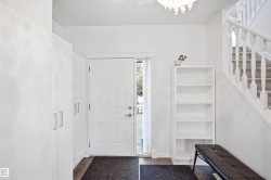 Entryway featuring a paneled door with sidelight, wood-finish flooring, built-in storage cabinetry with brushed nickel hardware, and a carpeted staircase with white balusters - 