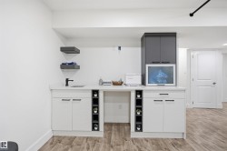 Integrated wet bar featuring a single basin sink with a matte black faucet, white shaker-style cabinetry, and a light-toned countertop - 