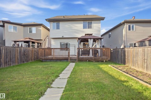 Expansive backyard featuring a manicured lawn, wood fencing, a raised garden bed, and a paved walkway leading to a spacious deck - 1523 36 Avenue Nw, Edmonton, AB 