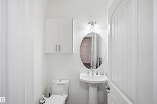 Pedestal sink, oval mirror, wall-mounted light fixture, and white cabinetry - 1523 36 Avenue Nw, Edmonton, AB 