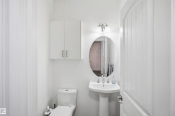 Pedestal sink, oval mirror, wall-mounted light fixture, and white cabinetry - 