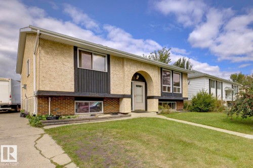 Stucco exterior with brick detailing, arched entry, multiple windows, and a front lawn - 3216 138 Avenue Nw, Edmonton, AB 