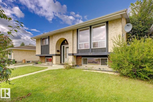 Stucco exterior featuring an arched entryway, multiple large windows, and a manicured front lawn with a concrete pathway - 3216 138 Avenue Nw, Edmonton, AB 