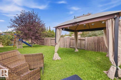 Expansive backyard featuring a lush lawn, privacy fencing, and a built-in gazebo with draped fabric sides - 3216 138 Avenue Nw, Edmonton, AB 