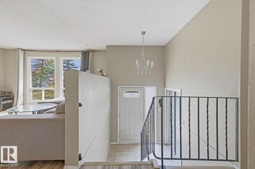 High ceilings with a decorative chandelier, white entry door with glass inserts, black metal railing, and large windows - 3216 138 Avenue Nw, Edmonton, AB 