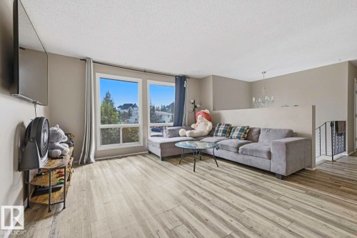 Wood-finish flooring, multiple windows, recessed staircase with wrought iron railing, and a modern chandelier - 3216 138 Avenue Nw, Edmonton, AB 