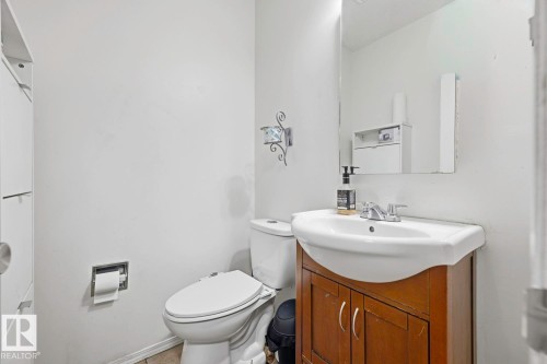 White ceramic toilet, wood-finish vanity with integrated sink, chrome faucet, and wall-mounted mirror - 3216 138 Avenue Nw, Edmonton, AB 