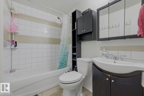 Bathroom featuring a bathtub with tile surround, toilet, vanity with integrated sink, and wall-mounted medicine cabinet - 3216 138 Avenue Nw, Edmonton, AB 