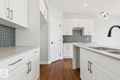 Crisp white cabinetry with brushed nickel hardware, light-toned countertops, a textured tile backsplash, a kitchen island with an undermount sink, and wood-finish flooring - 72 Maple Crescent, Gibbons, AB 