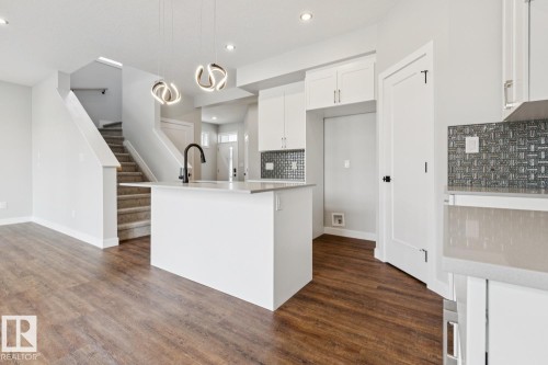 Wood-finish flooring, white kitchen cabinetry, kitchen island with sink, contemporary pendant lighting, and mosaic tile backsplash - 72 Maple Crescent, Gibbons, AB 