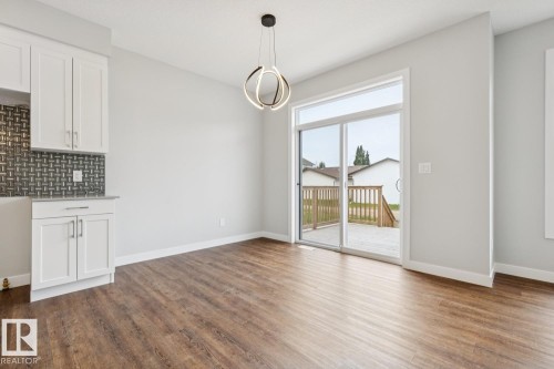 White cabinetry with a light stone-finish countertop, dark mosaic tile backsplash, wood-finish flooring, and a contemporary ceiling light fixture - 72 Maple Crescent, Gibbons, AB 