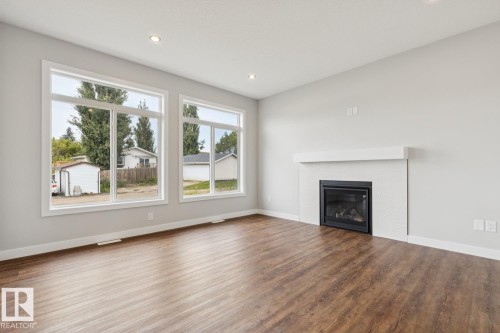 Warm wood-finish flooring, recessed lighting, and a modern fireplace with a white mantel and tiled surround - 72 Maple Crescent, Gibbons, AB 