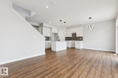 Expansive wood-finish flooring, white cabinetry, dark subway tile backsplash, and contemporary pendant lighting - 72 Maple Crescent, Gibbons, AB 