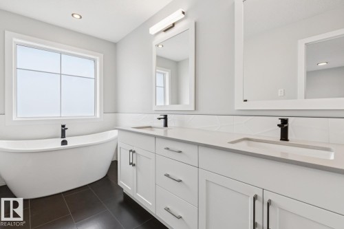 Freestanding soaking tub, dual vanity with undermount sinks, quartz countertops, black plumbing fixtures, and dark tile flooring - 72 Maple Crescent, Gibbons, AB 