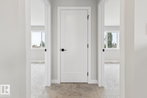 Hallway featuring light gray carpeting, white flat-panel doors with matte black hardware, and bright interior spaces with windows - 72 Maple Crescent, Gibbons, AB 