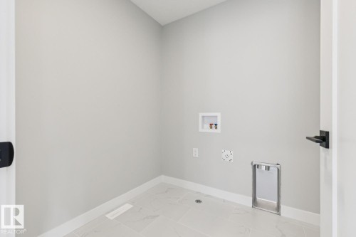 Laundry area with light-toned walls, tile flooring, and matte black hardware - 72 Maple Crescent, Gibbons, AB 