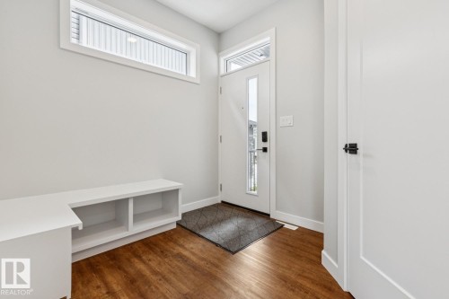 Wood-finish flooring, white built-in bench with cubbies, transom window, entry door with frosted glass insert, and matte black door hardware - 72 Maple Crescent, Gibbons, AB 