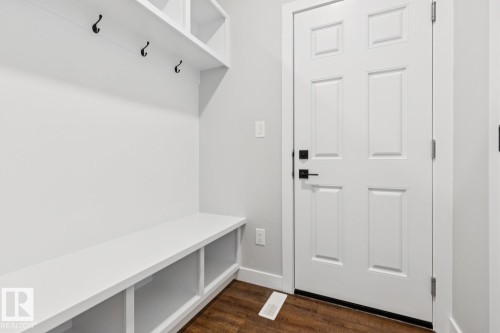 Built-in storage bench with open shelving, wall-mounted coat hooks, overhead shelving, paneled door, and wood-finish flooring - 72 Maple Crescent, Gibbons, AB 