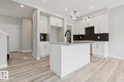 Kitchen featuring a central island, white cabinetry, dark herringbone tile backsplash, and contemporary pendant lighting - 36 Maple Crescent, Gibbons, AB 