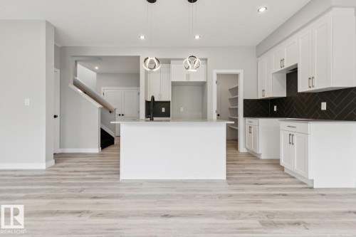 Modern kitchen featuring white cabinetry, a large island, black herringbone backsplash, wood-finish flooring, and pendant lighting - 36 Maple Crescent, Gibbons, AB 