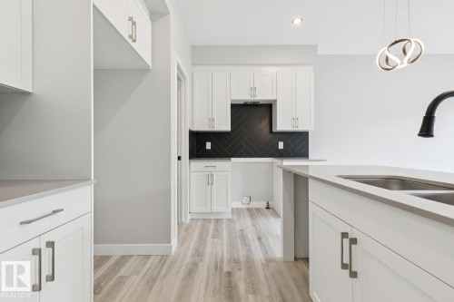 Contemporary kitchen featuring white cabinetry, wood-finish flooring, a herringbone tile backsplash, a kitchen island with an undermount sink, and recessed lighting - 36 Maple Crescent, Gibbons, AB 