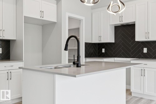White shaker cabinetry, light-toned countertops, black herringbone tile backsplash, and a matte black gooseneck faucet - 36 Maple Crescent, Gibbons, AB 