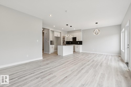 Light wood-finish flooring throughout, recessed ceiling lighting, contemporary pendant lights, white cabinetry with black hardware, and an island with an integrated sink - 36 Maple Crescent, Gibbons, AB 