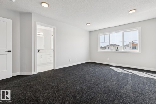 Spacious room featuring neutral paint, recessed lighting, a large window, dark carpeting, and a white interior door with black hardware - 36 Maple Crescent, Gibbons, AB 