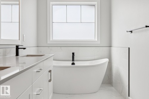 Freestanding soaking tub, dual vanity with undermount sinks, quartz countertop, matte black fixtures, and white tiled walls - 36 Maple Crescent, Gibbons, AB 