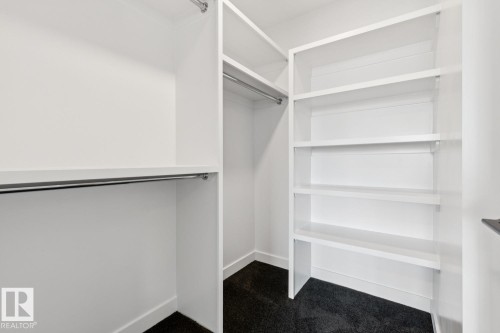 Built-in closet organization featuring multiple shelving units, integrated hanging rods, and dark carpeting - 36 Maple Crescent, Gibbons, AB 