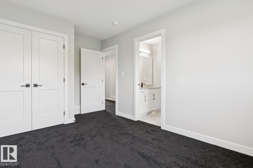 Plush dark carpeting, white shaker-style doors with black hardware, and an en-suite bathroom featuring a vanity with integrated lighting - 36 Maple Crescent, Gibbons, AB 